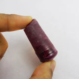 Purple cylindrical object held between fingers against a white background
