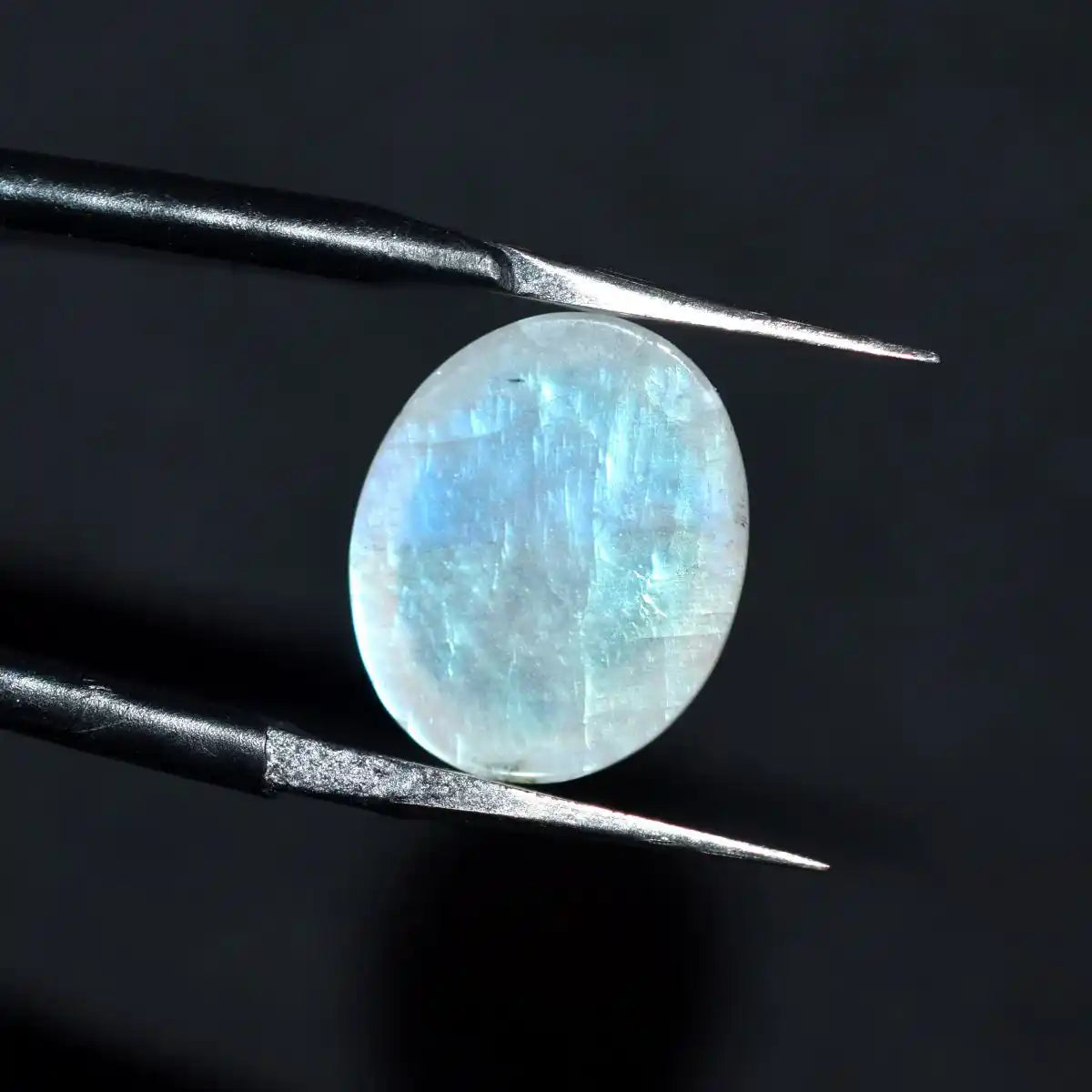 Round gemstone held by tweezers against a dark background