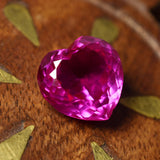 Polished 10.30 carat heart cut ruby in pink-red hue placed on patterned surface – eye-clean and certified