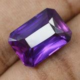 Rare Purple Tanzanite Emerald Cut Gemstone 12 Ct Held Between Fingers – Certified