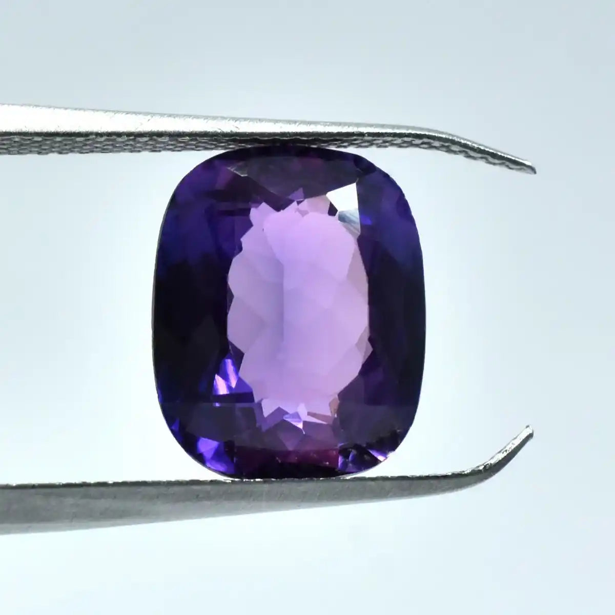 Purple gemstone held between tweezers on a light gray background