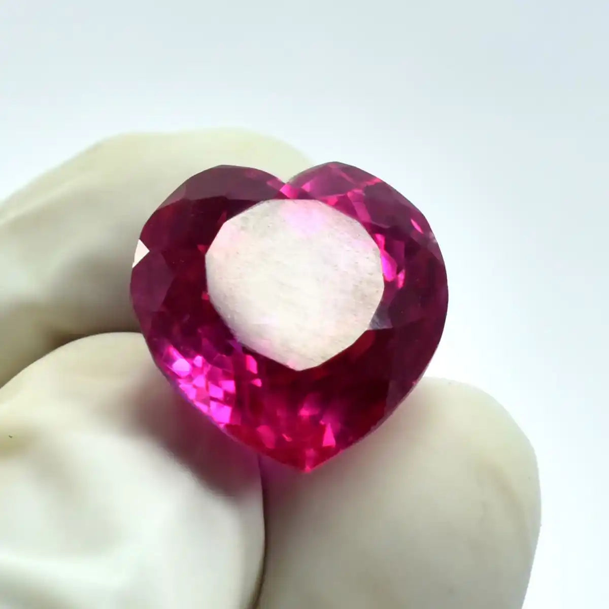 Heart-shaped pink gemstone held between two fingers on a white background
