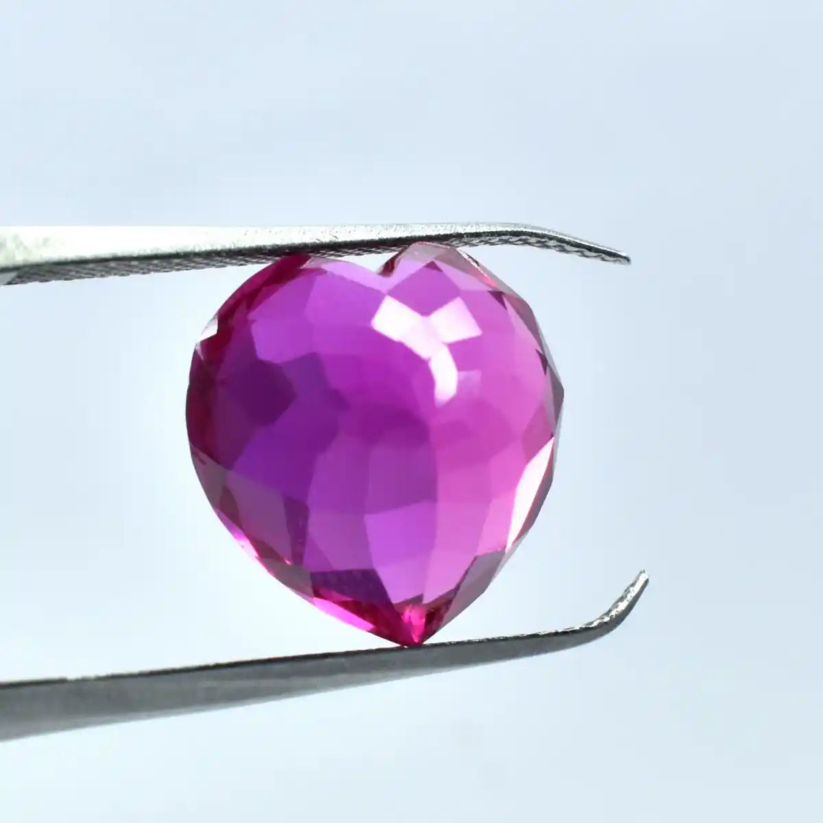 Faceted pink gemstone held between tweezers against a light blue background