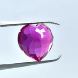 Faceted pink gemstone held between tweezers against a light blue background