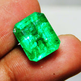 Natural green emerald gemstone with eye-clean clarity and rectangular shape viewed from top while held in fingers