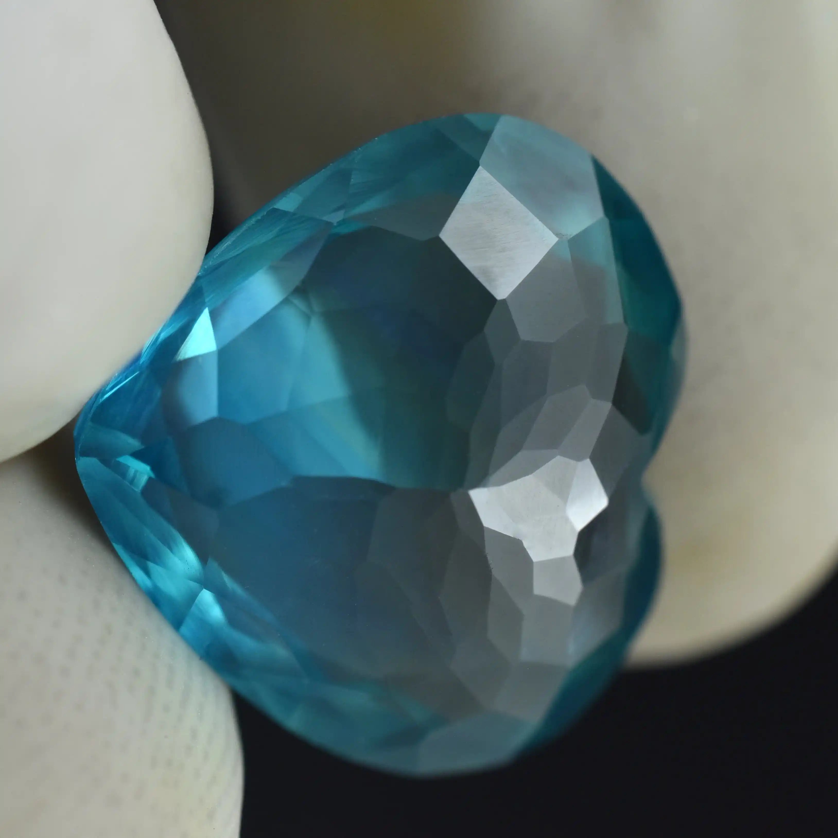 Faceted blue gemstone held by tweezers against a neutral background