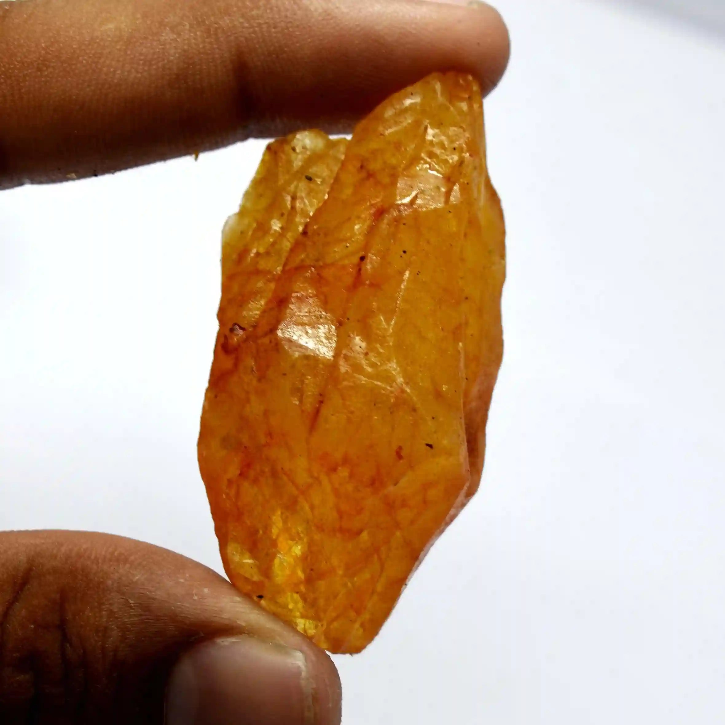 Hand holding a large orange crystal against a white background