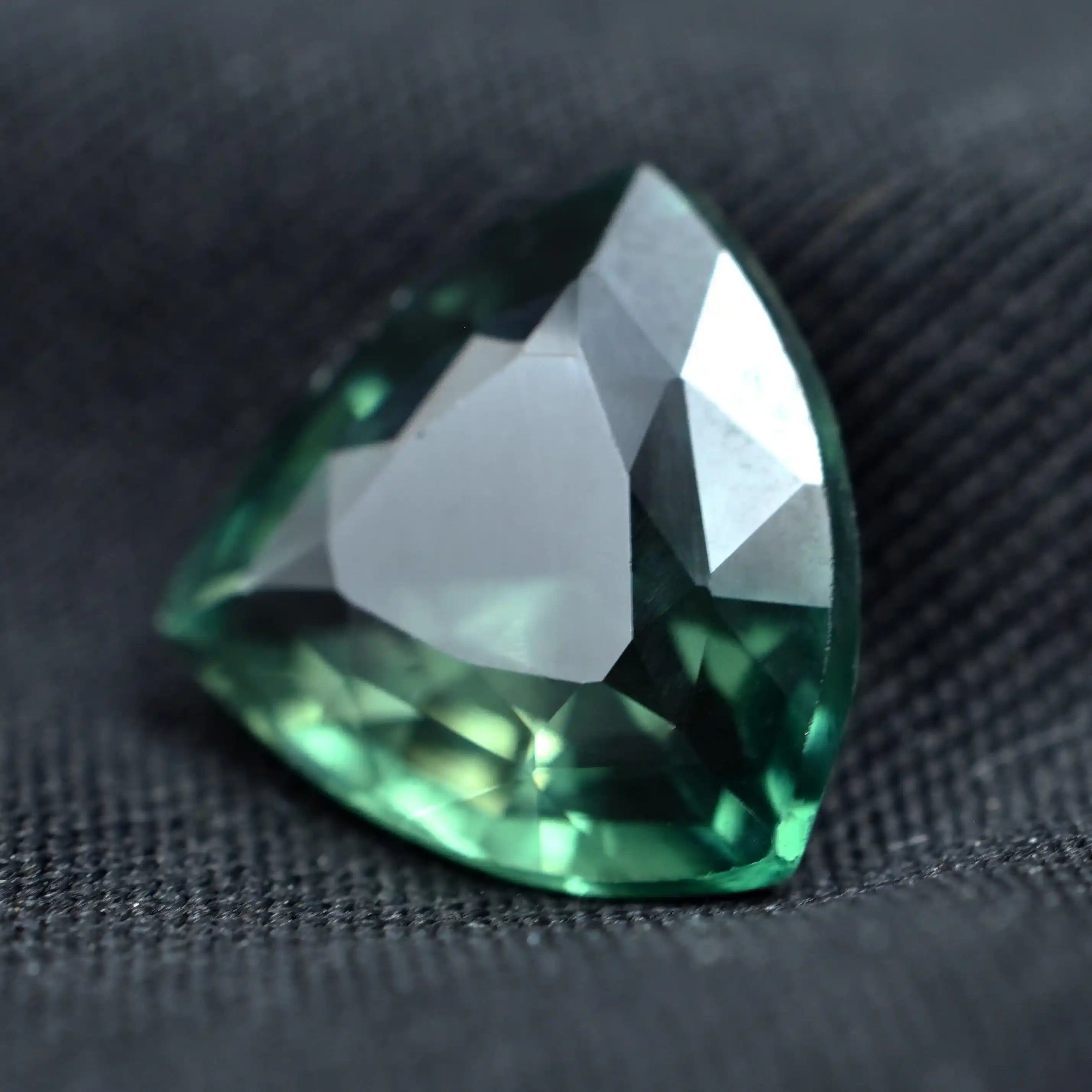 Faceted green gemstone on a dark fabric background