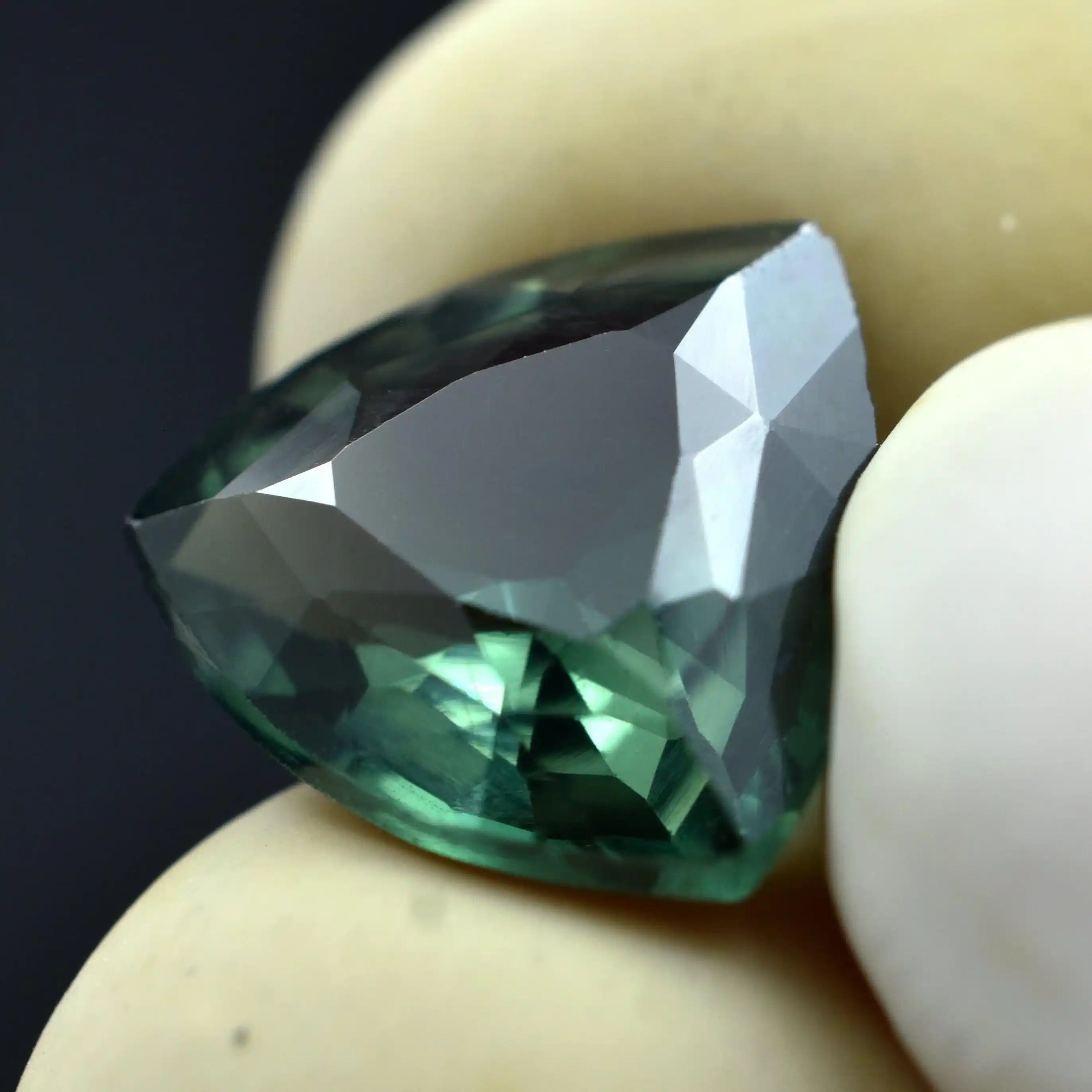 Faceted green gemstone held between two fingers against a dark background