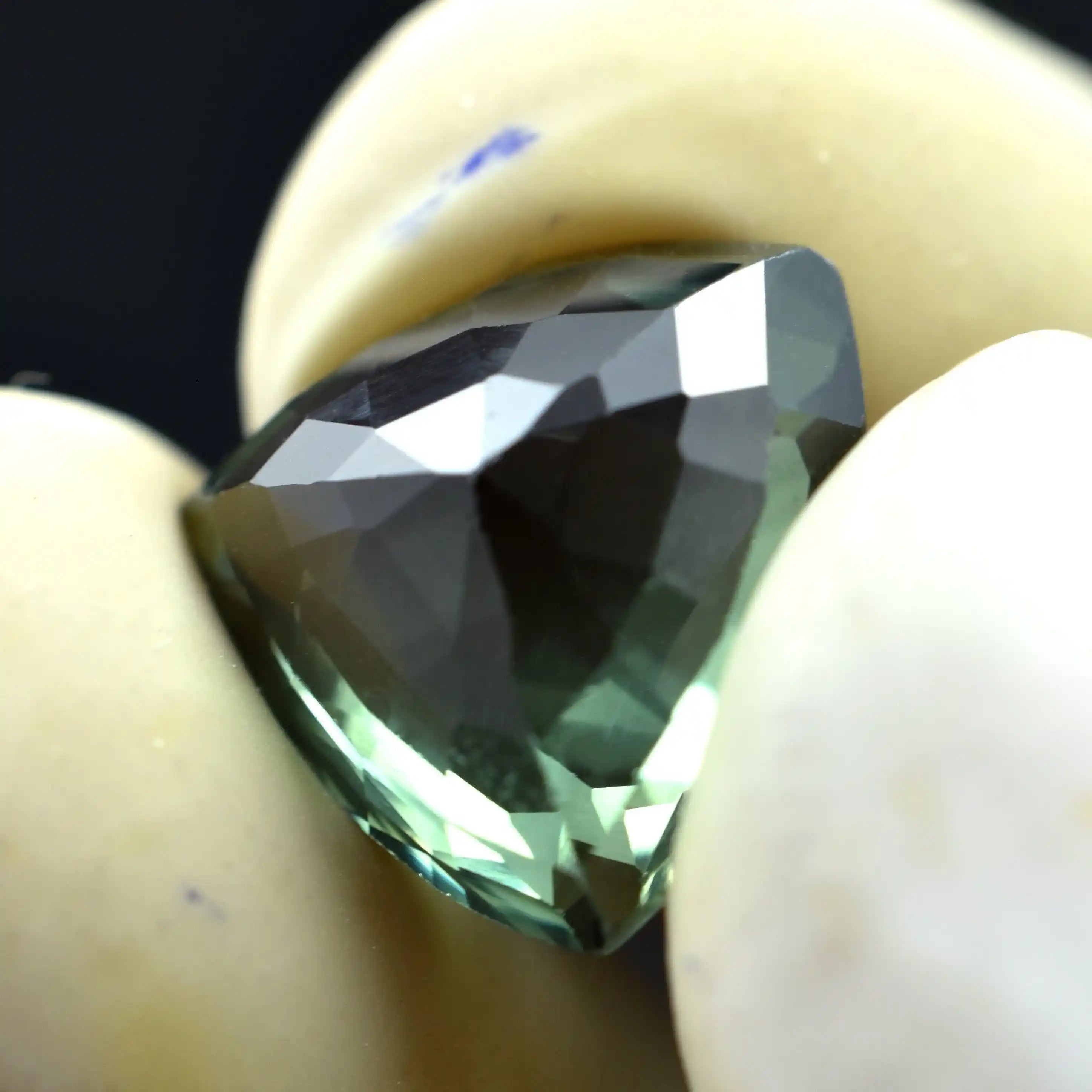 Faceted green gemstone held between two fingers against a dark background