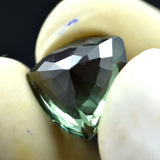 Faceted green gemstone held between two fingers against a dark background