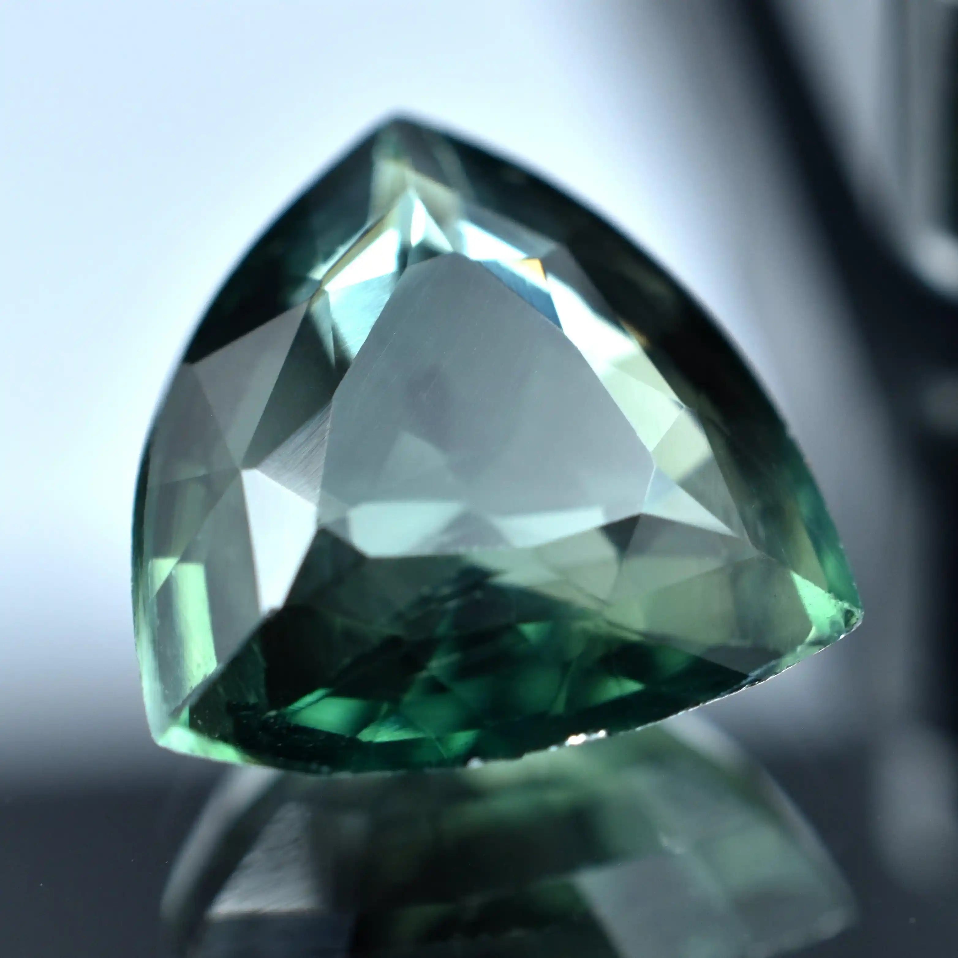 Trillion-cut green gemstone on a reflective surface with a blurred background