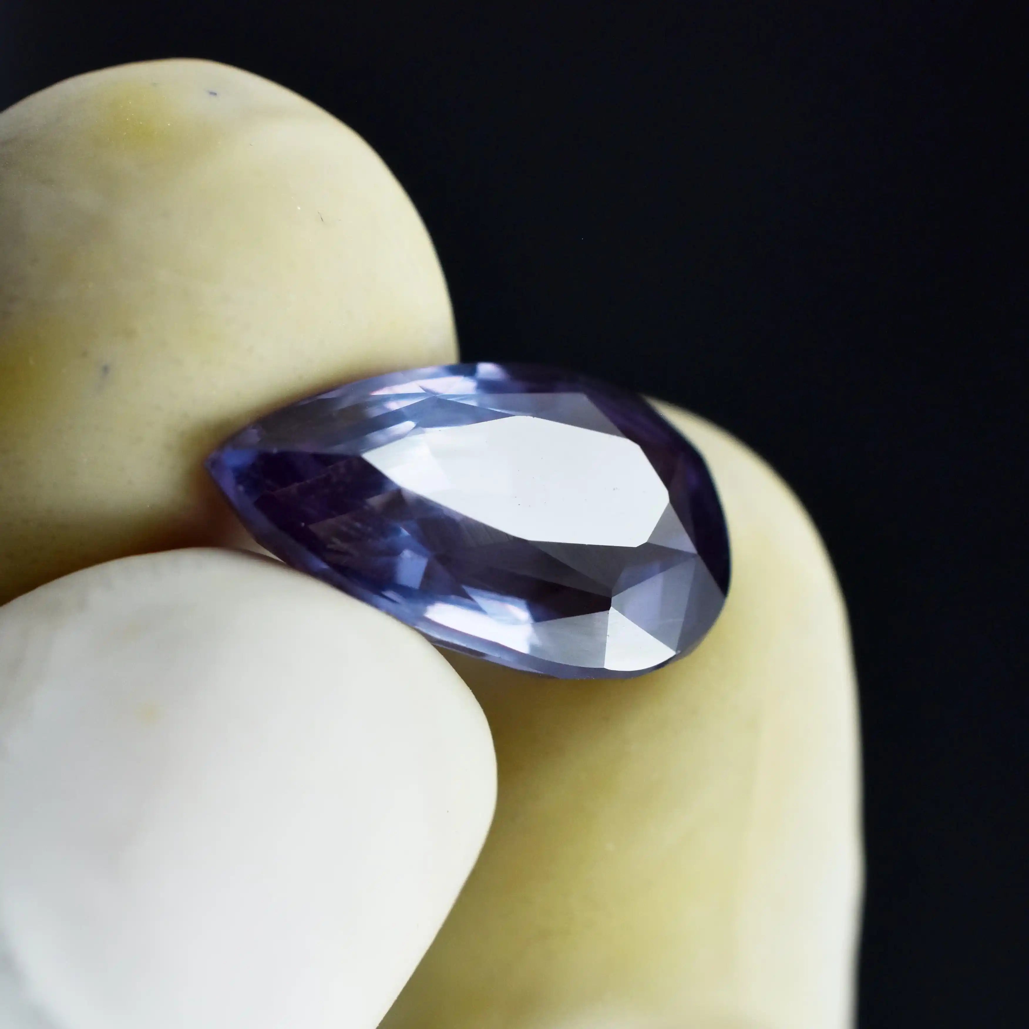 Faceted purple gemstone held between two hands against a dark background