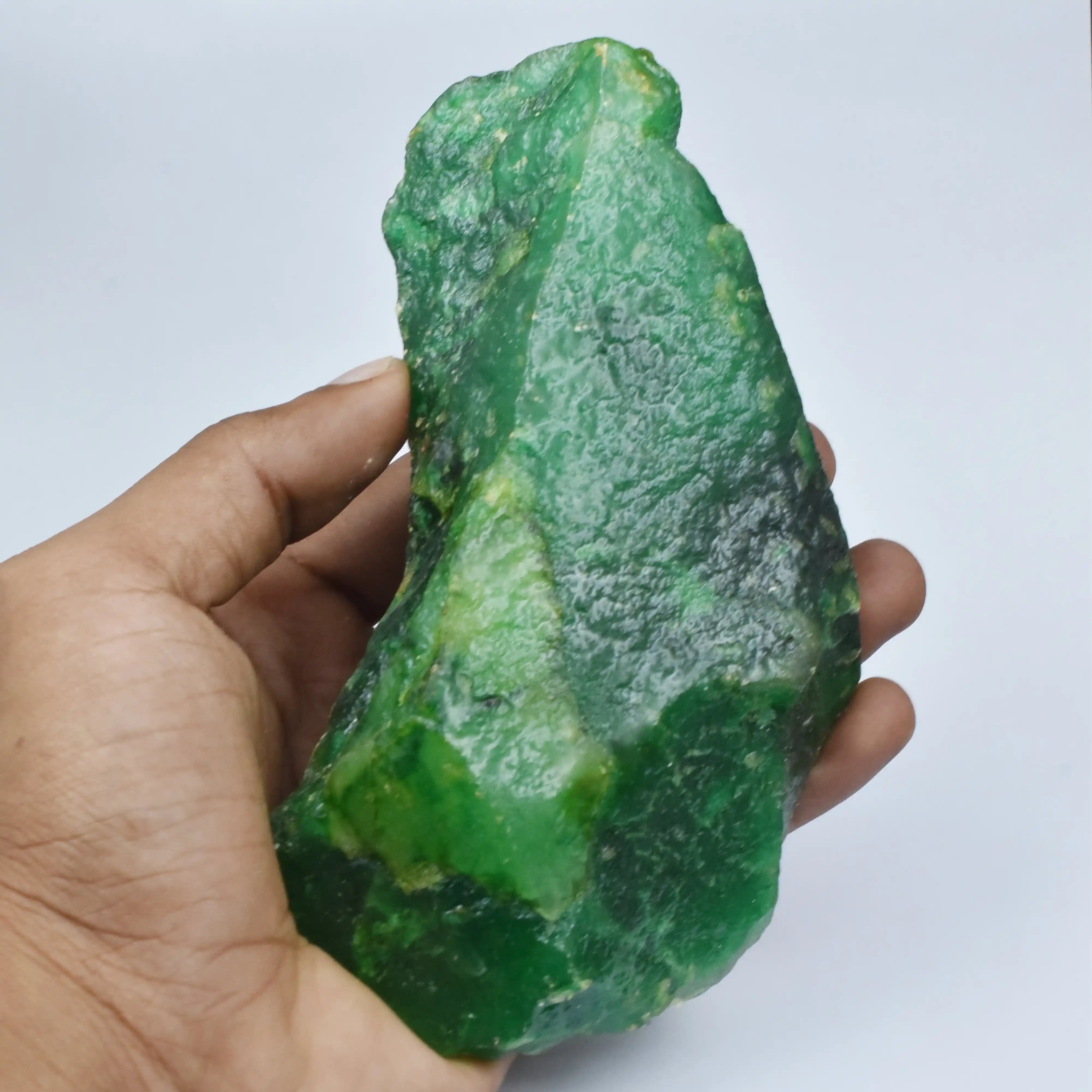 Hand holding a large green mineral stone against a light gray background