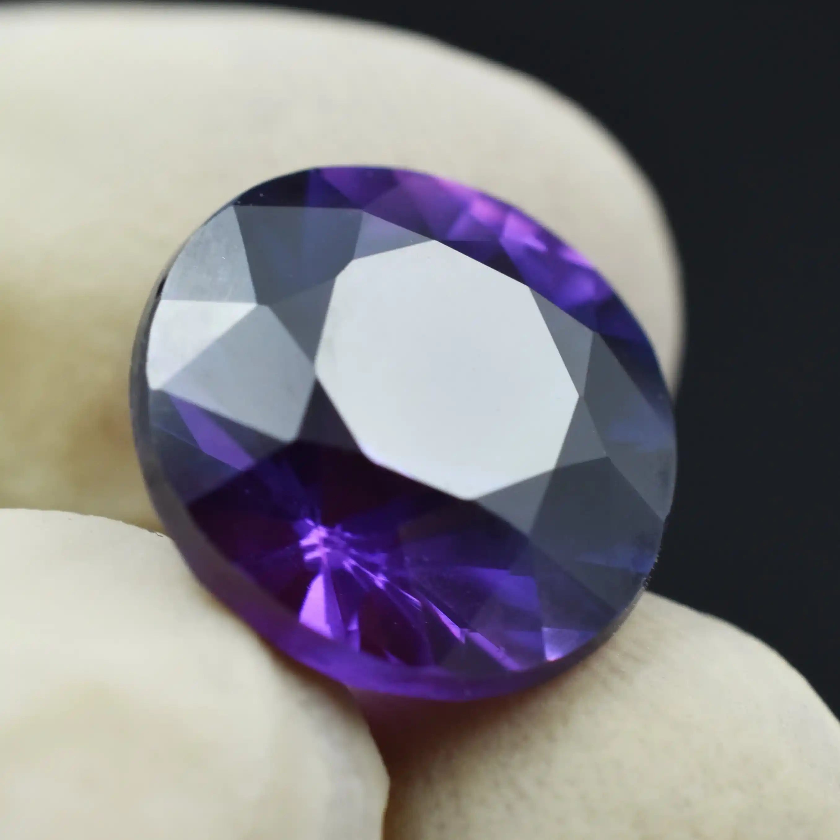 Faceted purple gemstone held between fingers against a dark background