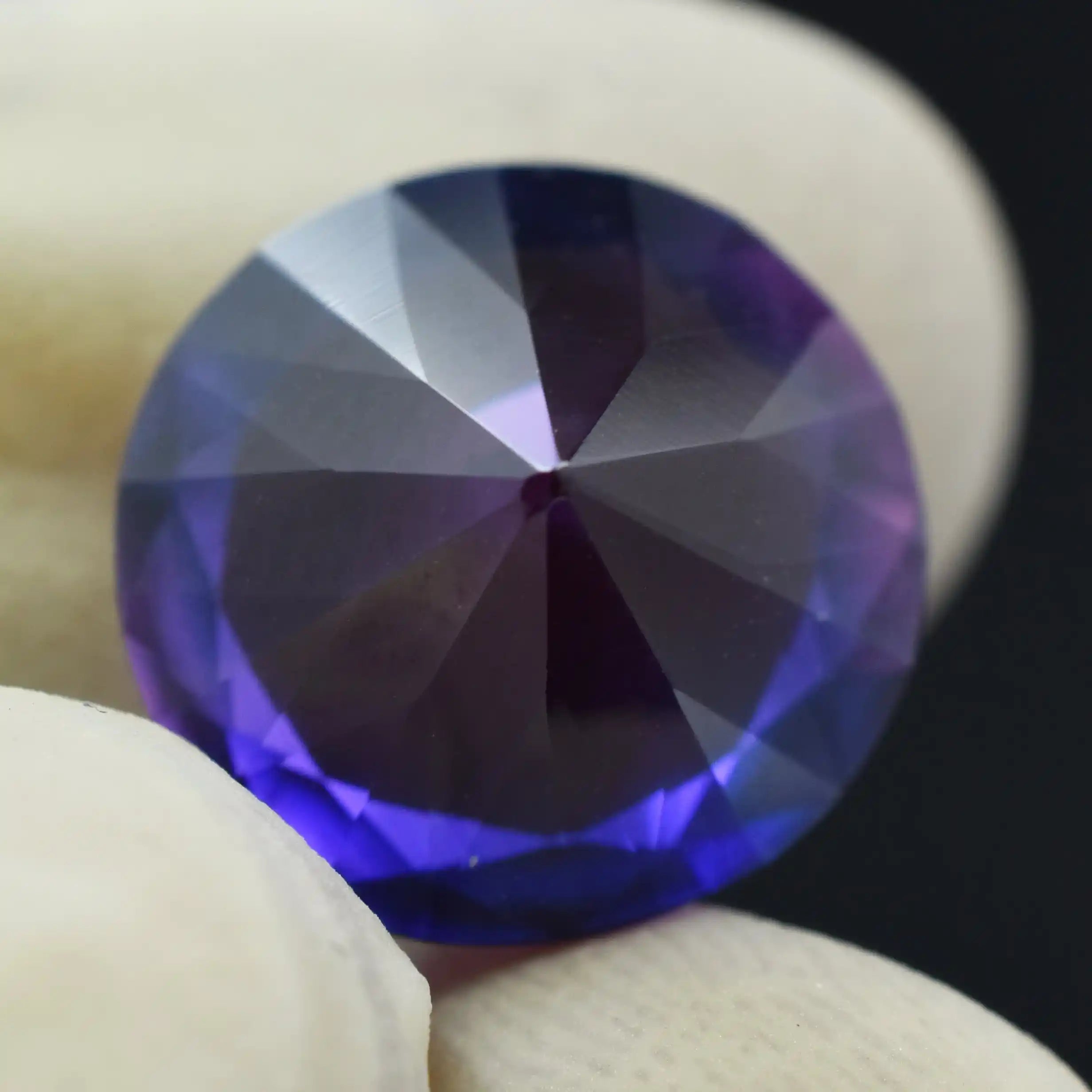 Close-up of a purple gemstone held between two fingers against a dark background