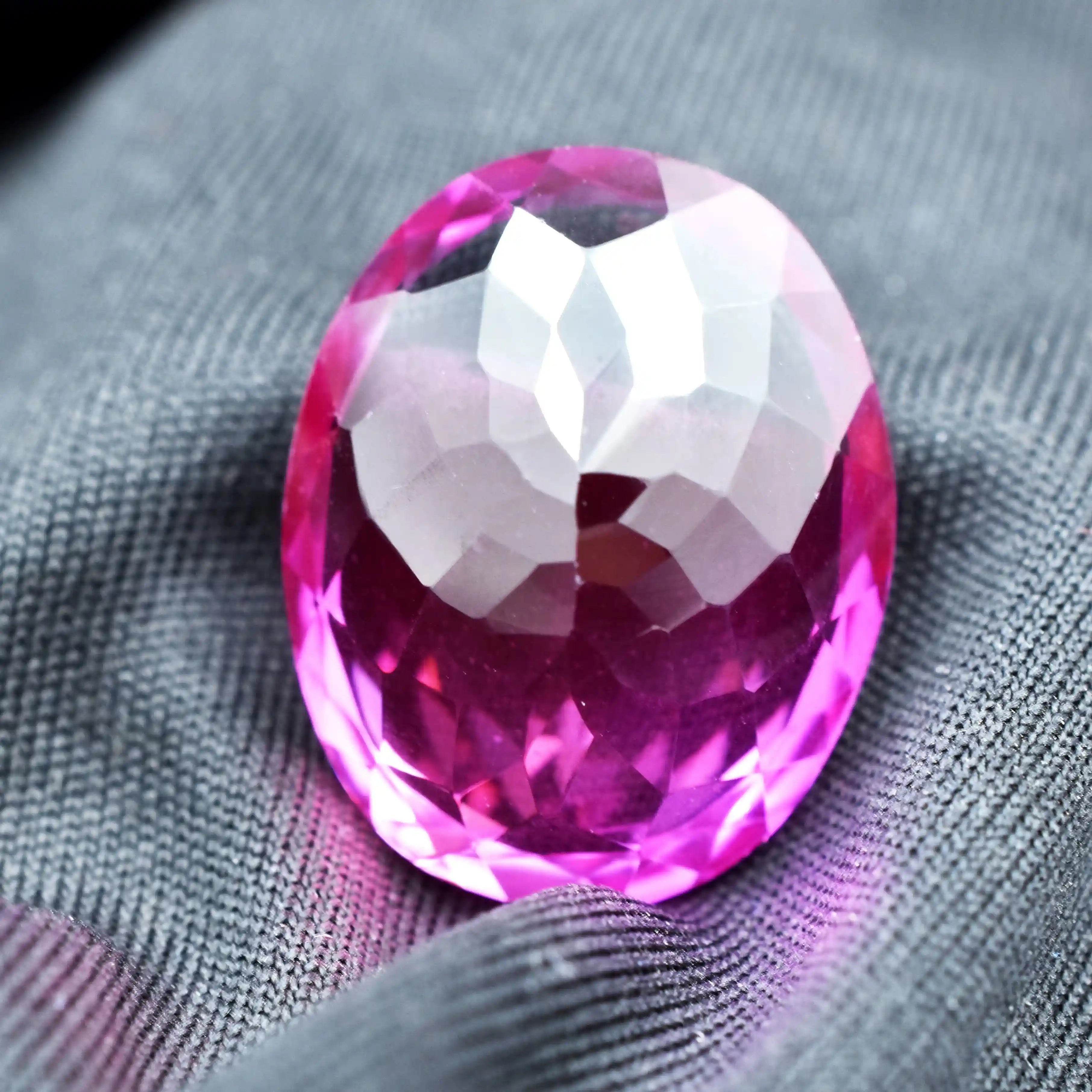 Faceted pink gemstone on a gray fabric background