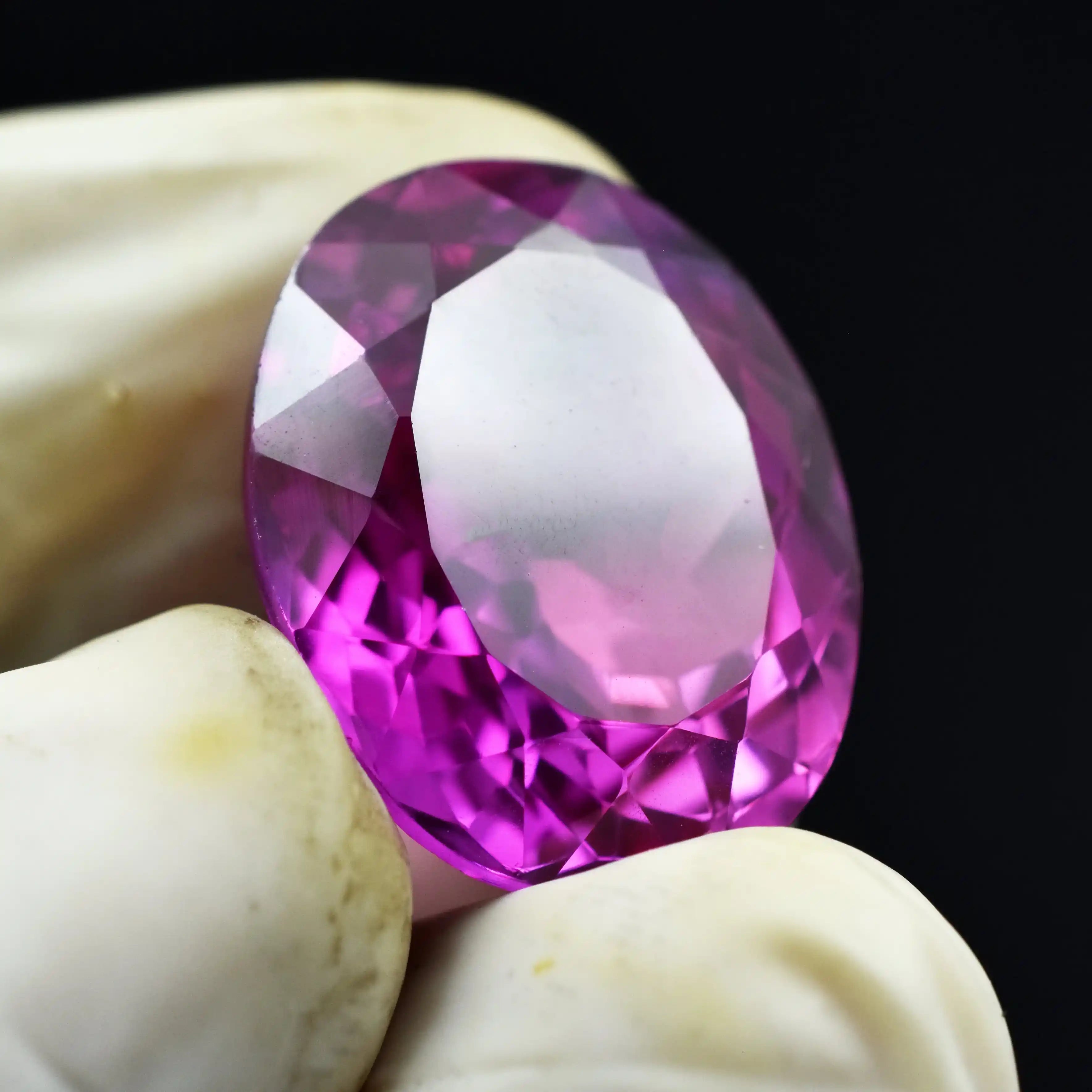 Close-up of a pink gemstone held between two fingers against a black background