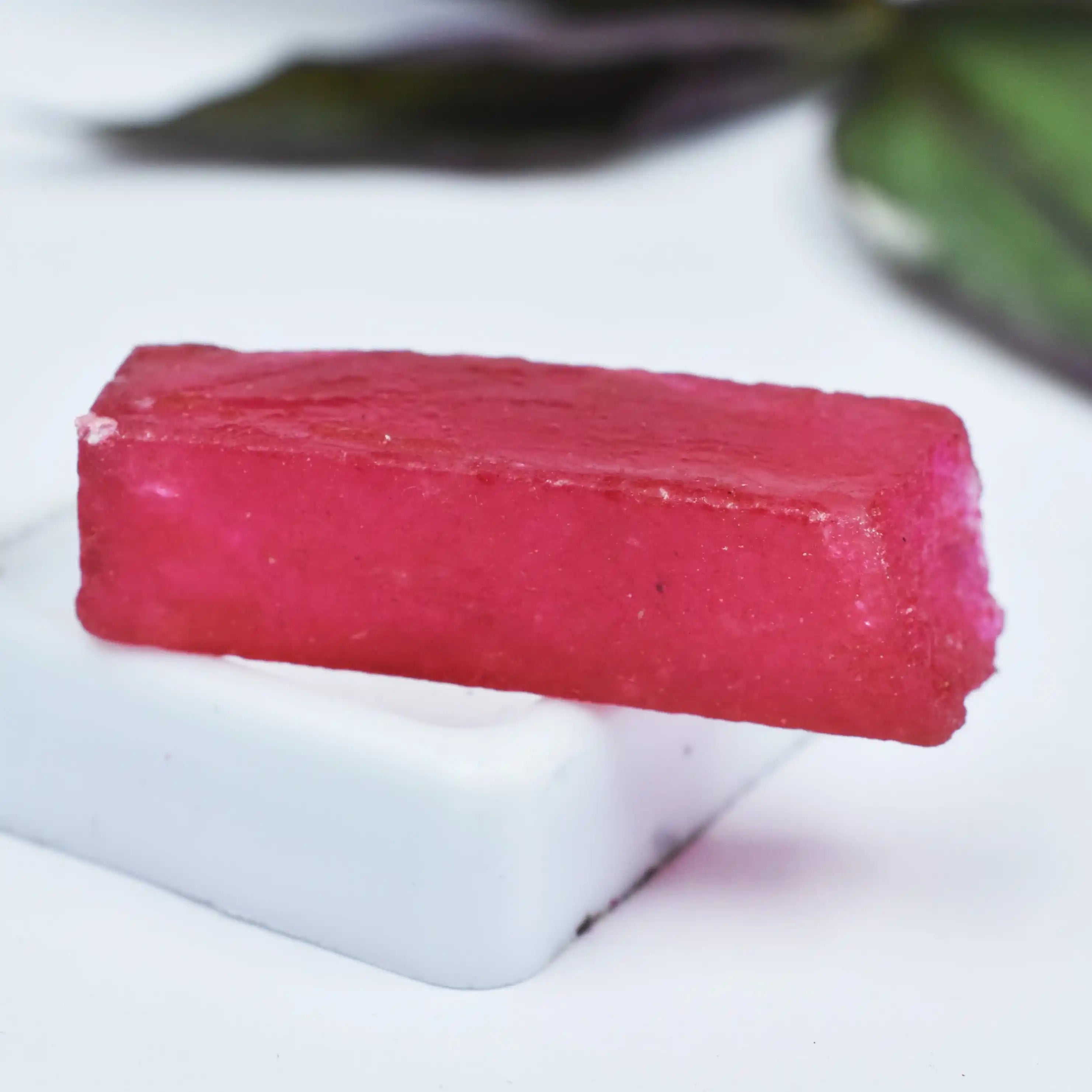 Pink rectangular soap bar on a white surface with a blurred green leafy background