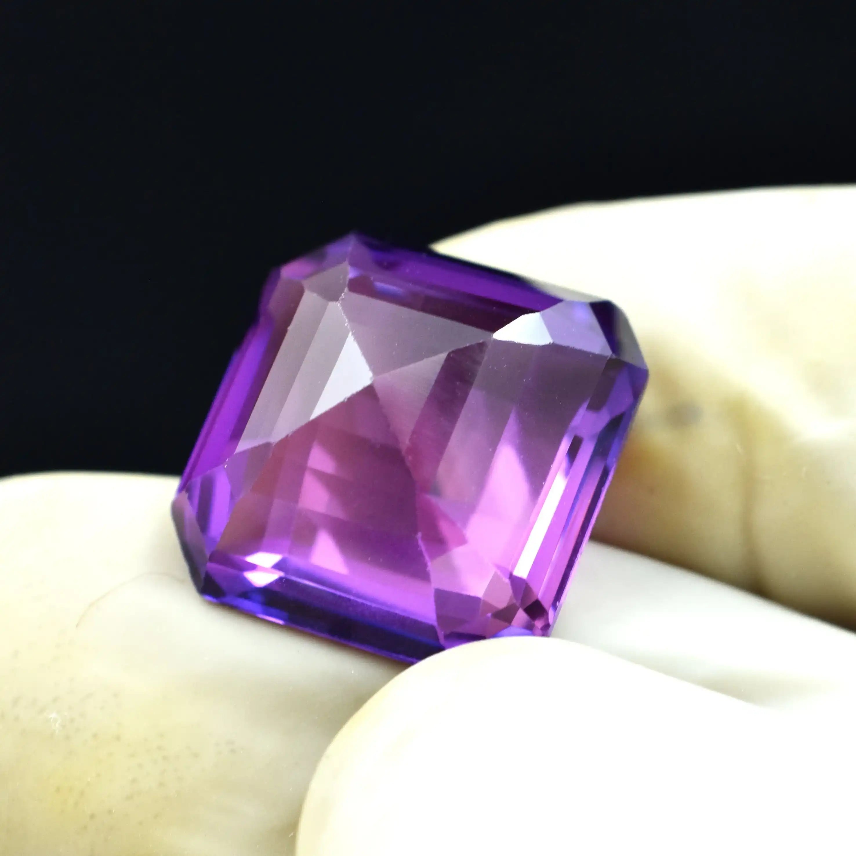 Faceted purple gemstone on a white surface with a black background