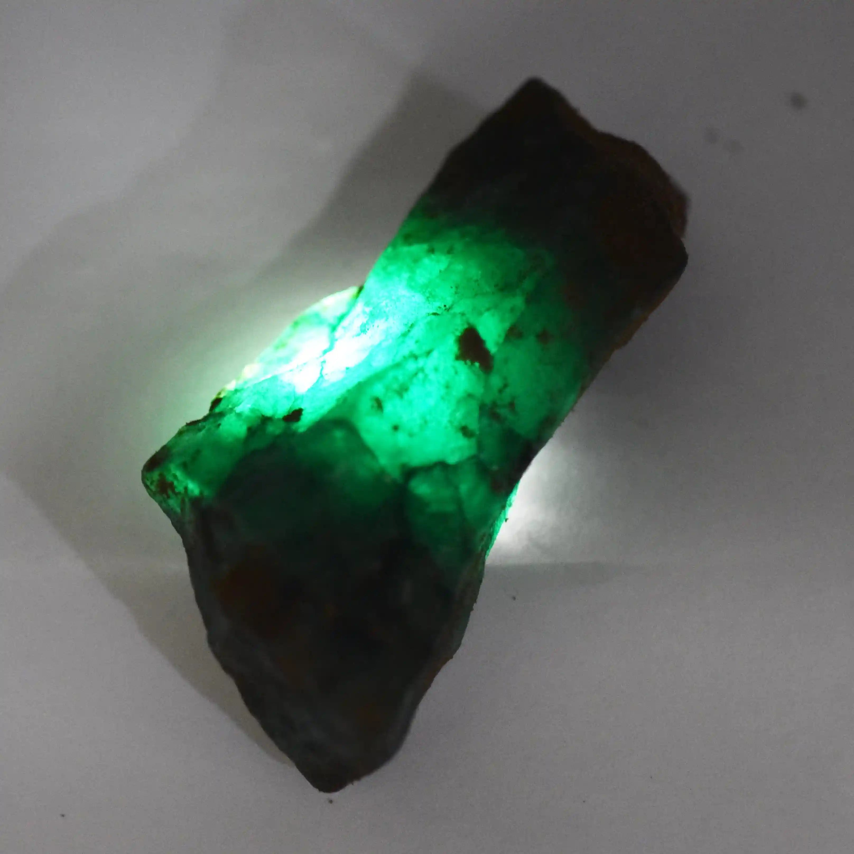 “Uncut emerald-like stone showing strong green illumination through its rough texture.”