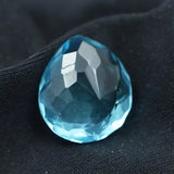 “Faceted blue pear-shaped gemstone placed on black fabric background.”