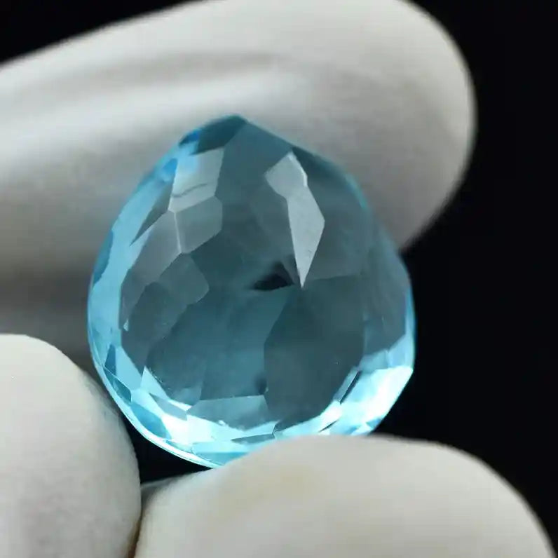 “Shiny blue gemstone with multiple facets photographed against black material.”