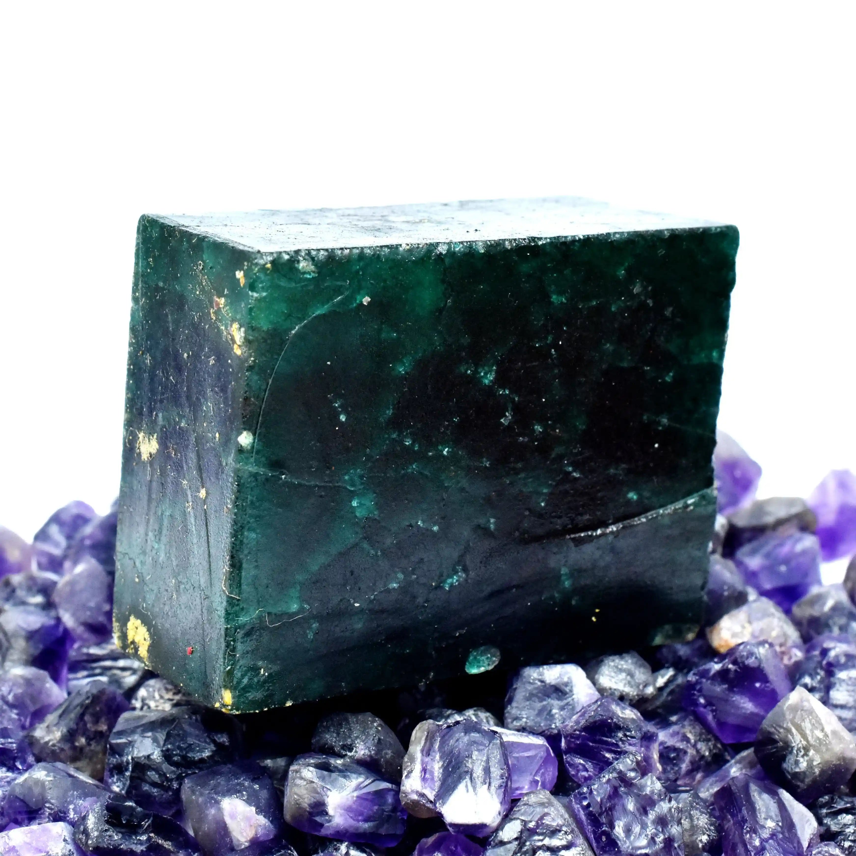 “Rough green stone specimen showcased against a background of raw purple crystals.”