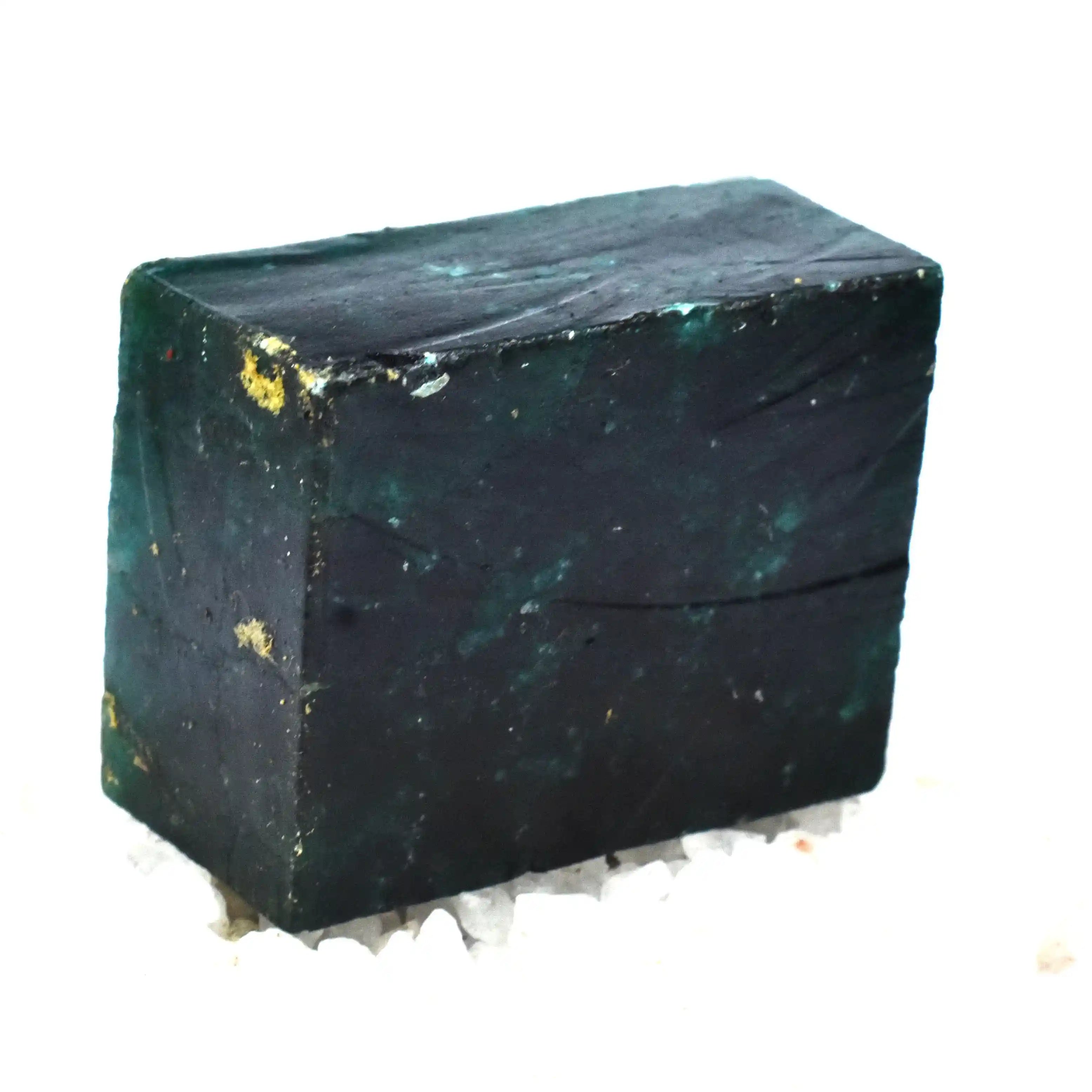 “Raw rectangular green crystal chunk displayed over scattered purple rough stones.”