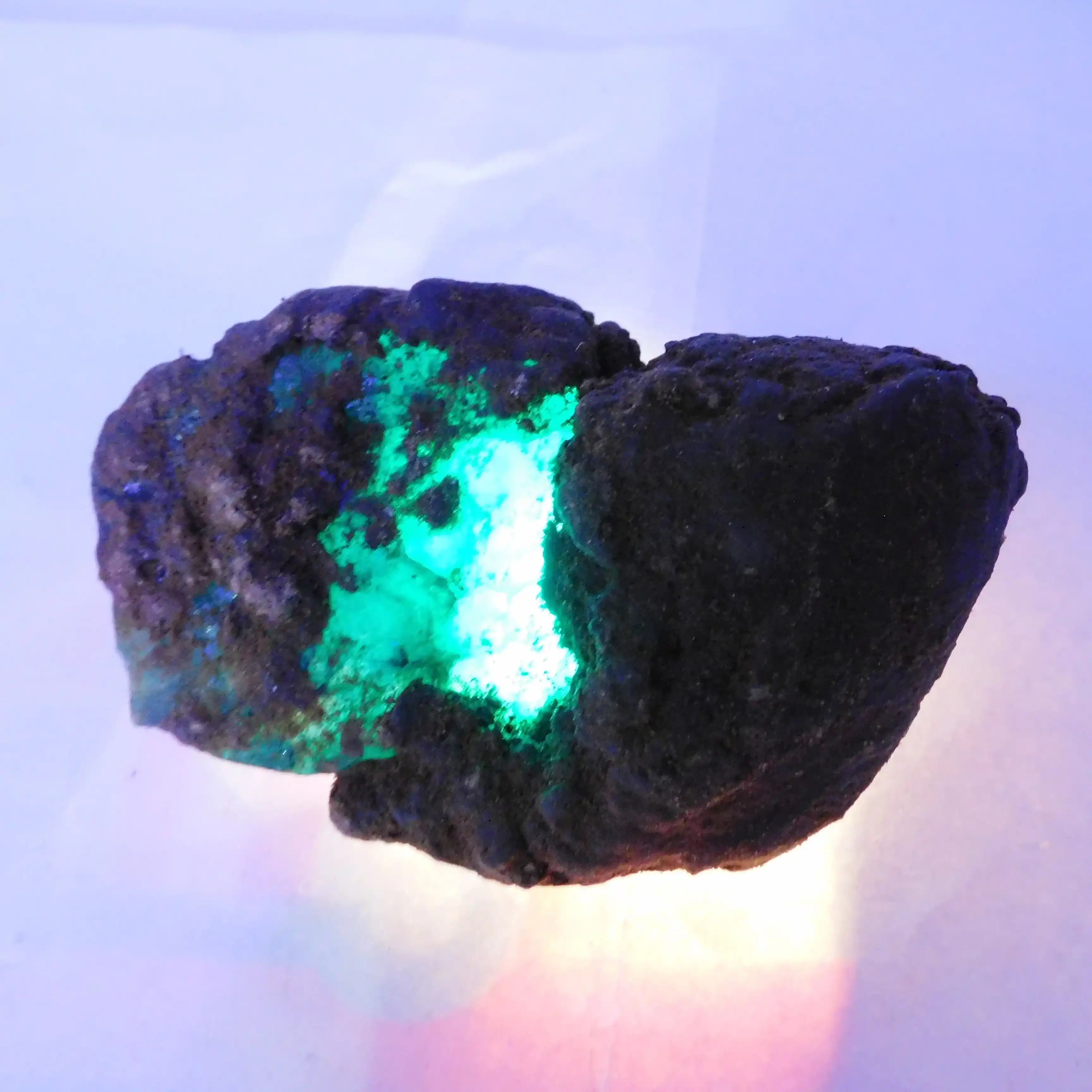 Mineral specimen with glowing green interior on a light blue background