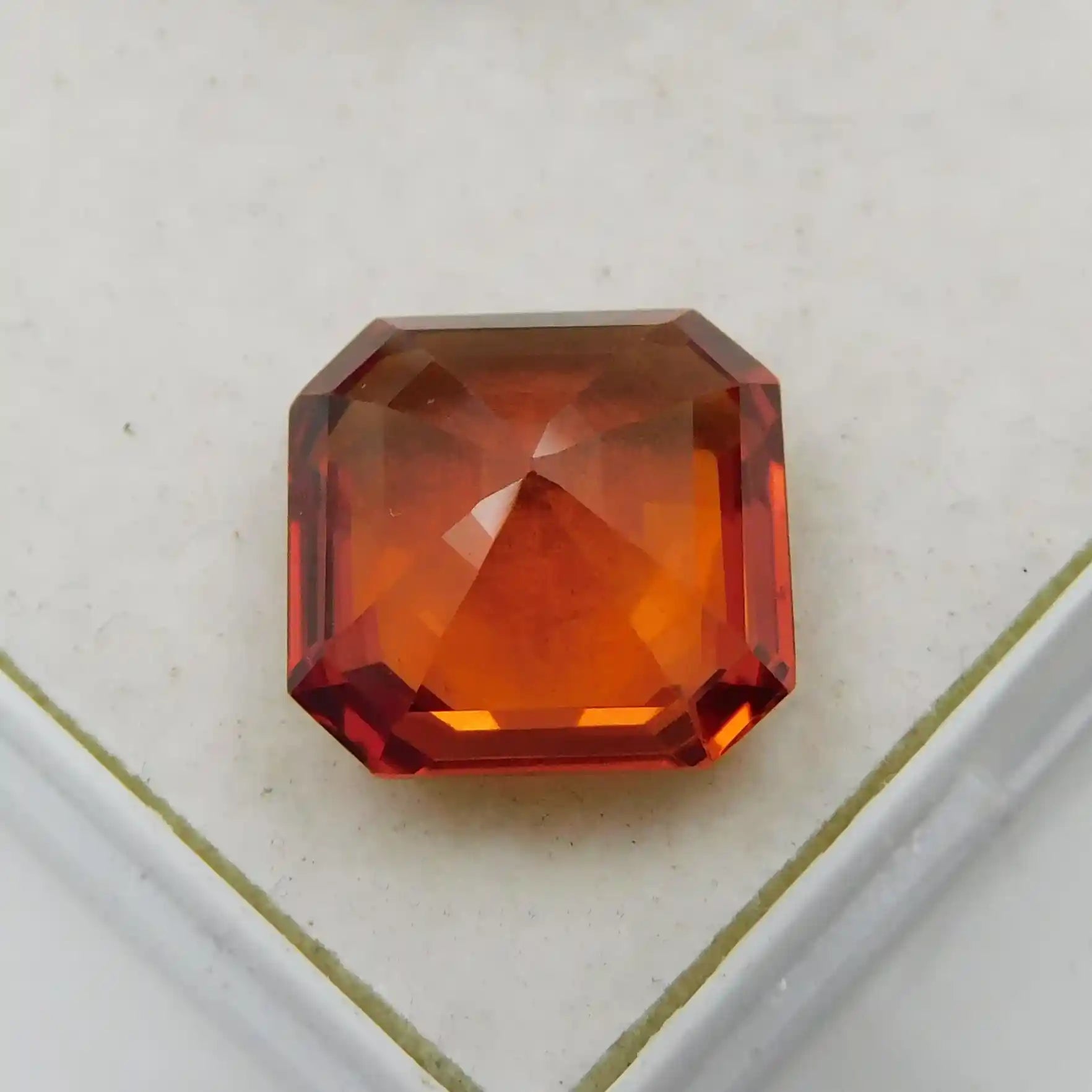 Faceted red-orange gemstone on a light beige background