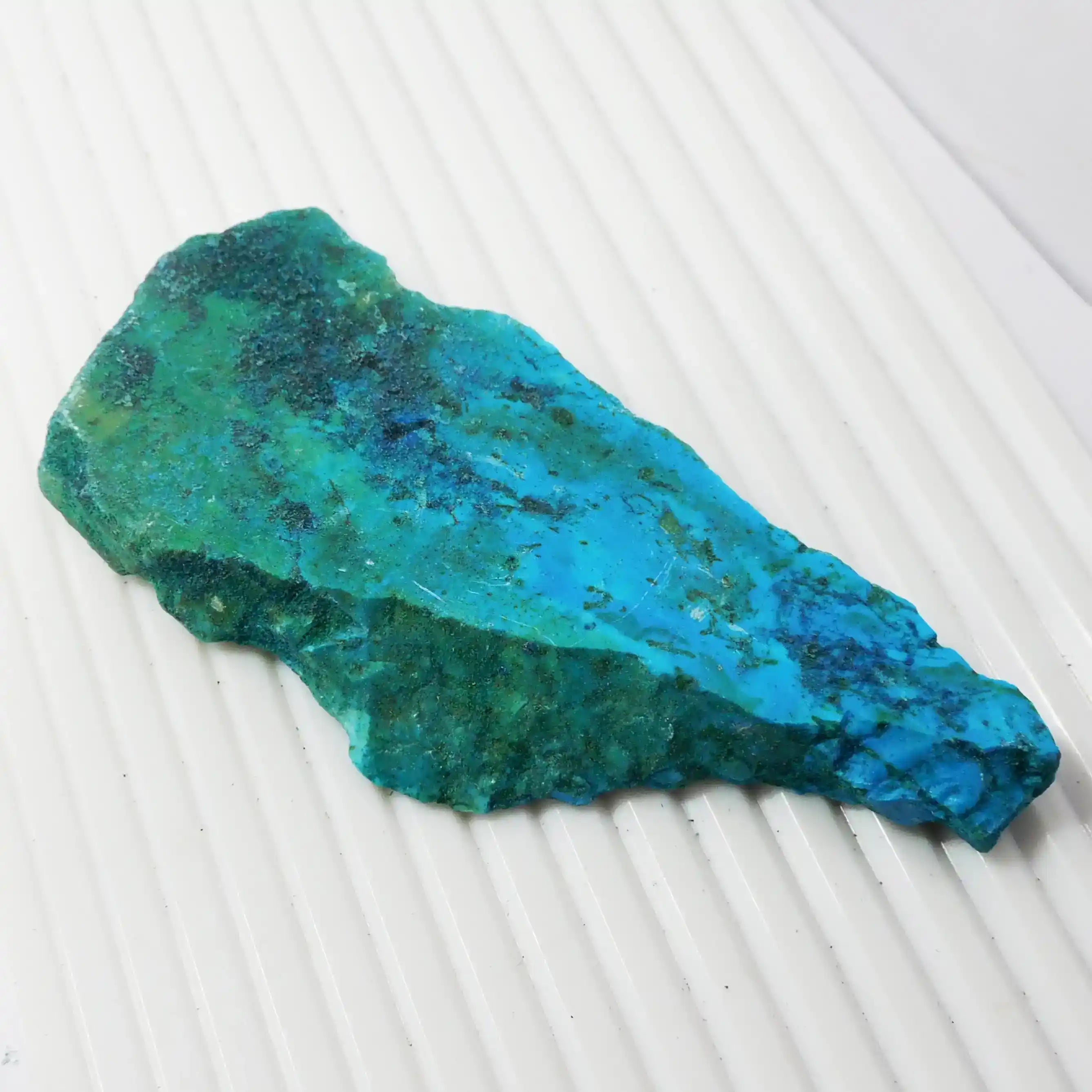 Blue-green mineral stone on a white textured surface