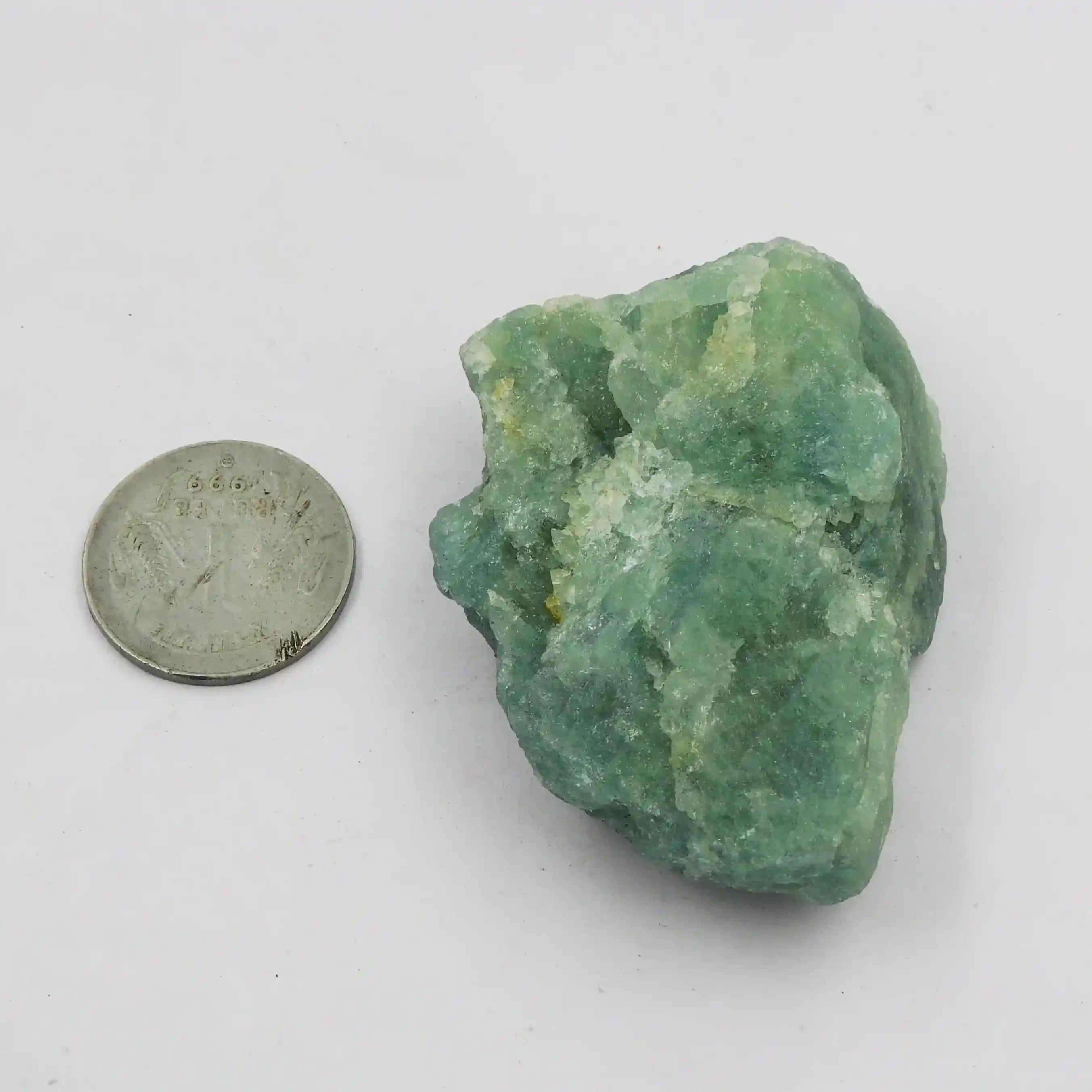 Green mineral rock next to a coin on a white background