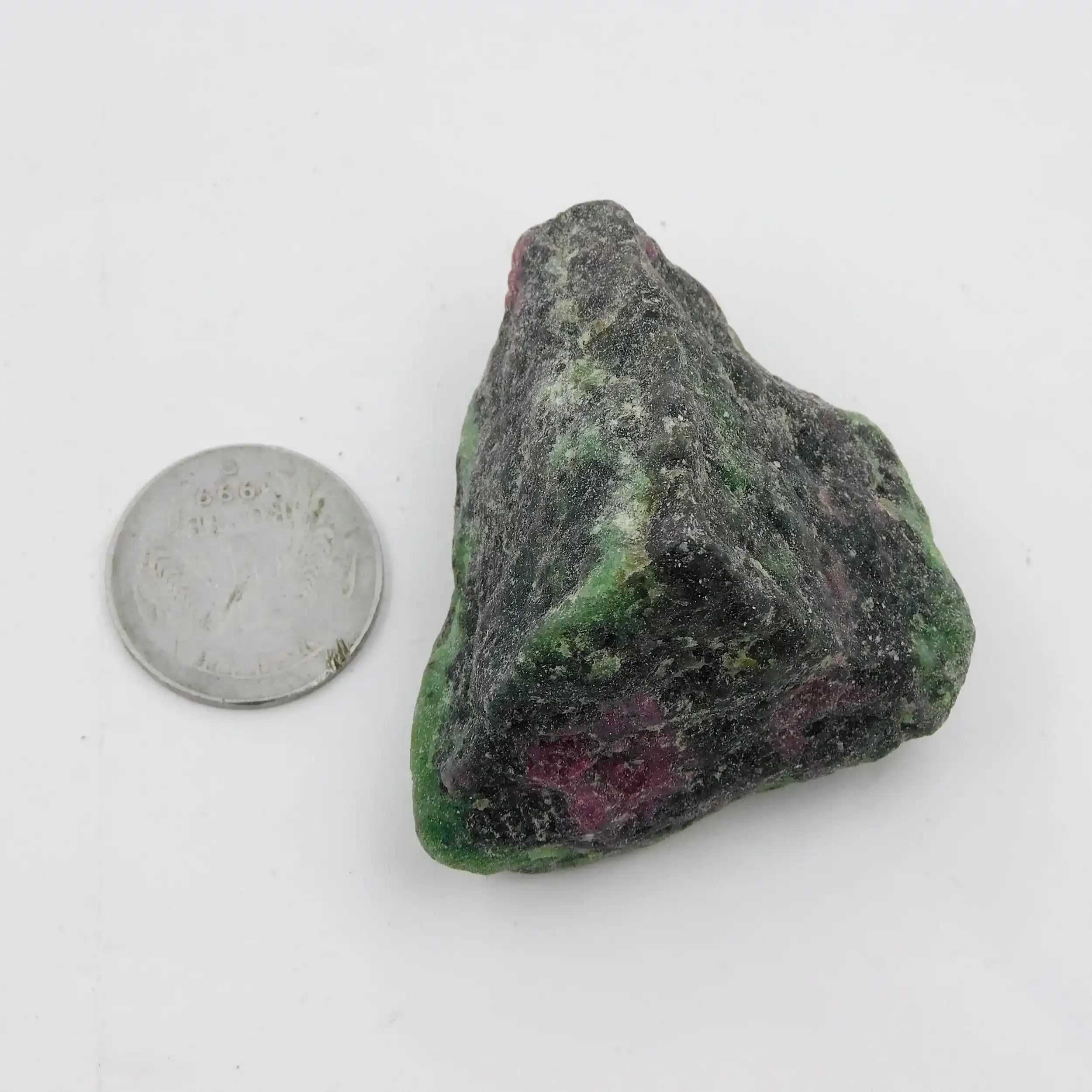 Raw ruby zoisite stone next to a quarter on a white background