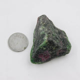 Raw ruby zoisite stone next to a quarter on a white background