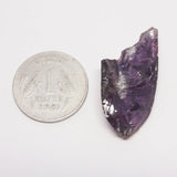 Amethyst crystal next to a silver rupee coin on a white background