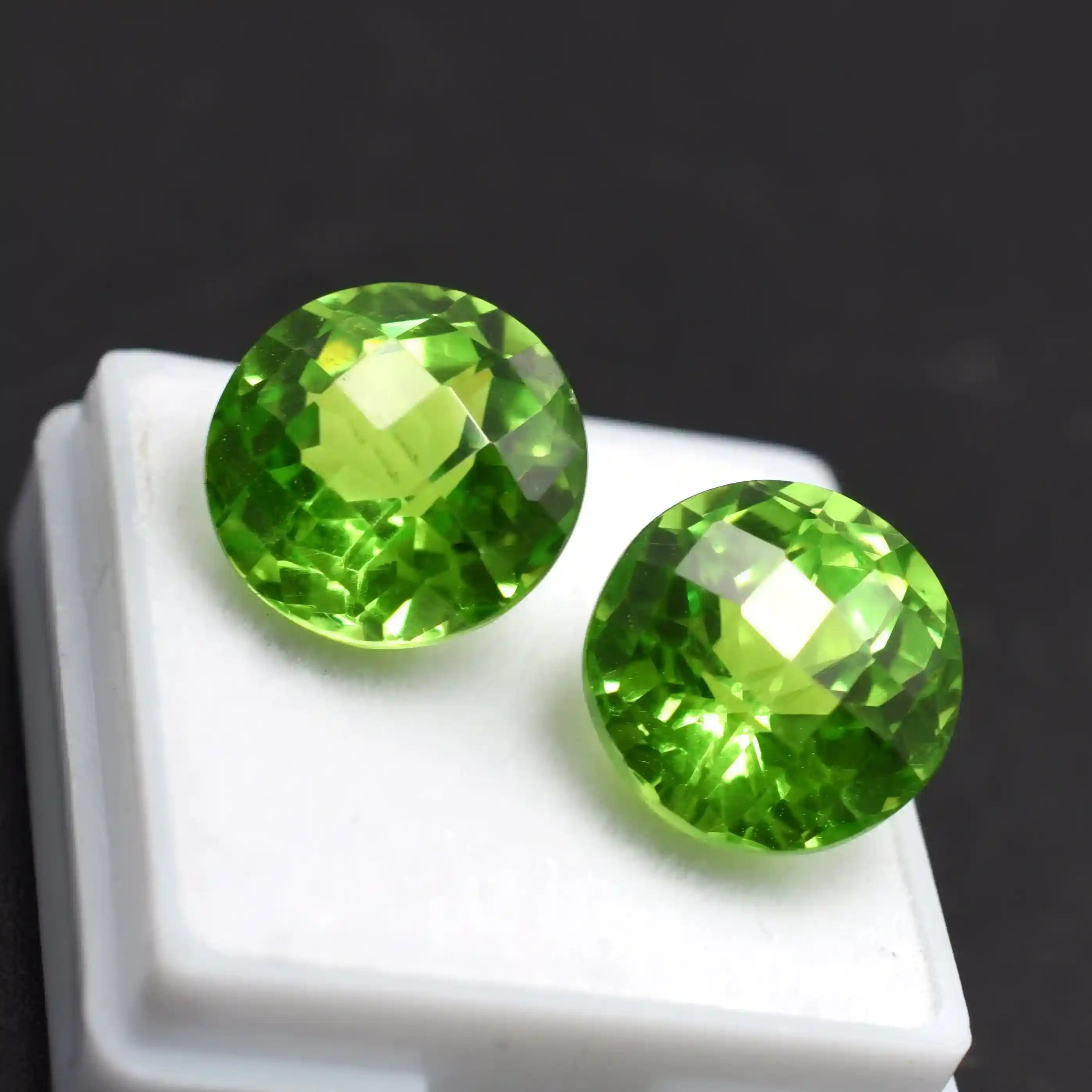Two green gemstones on a white stand with a dark background