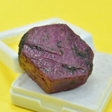 Purple mineral specimen on a white stand against a yellow background
