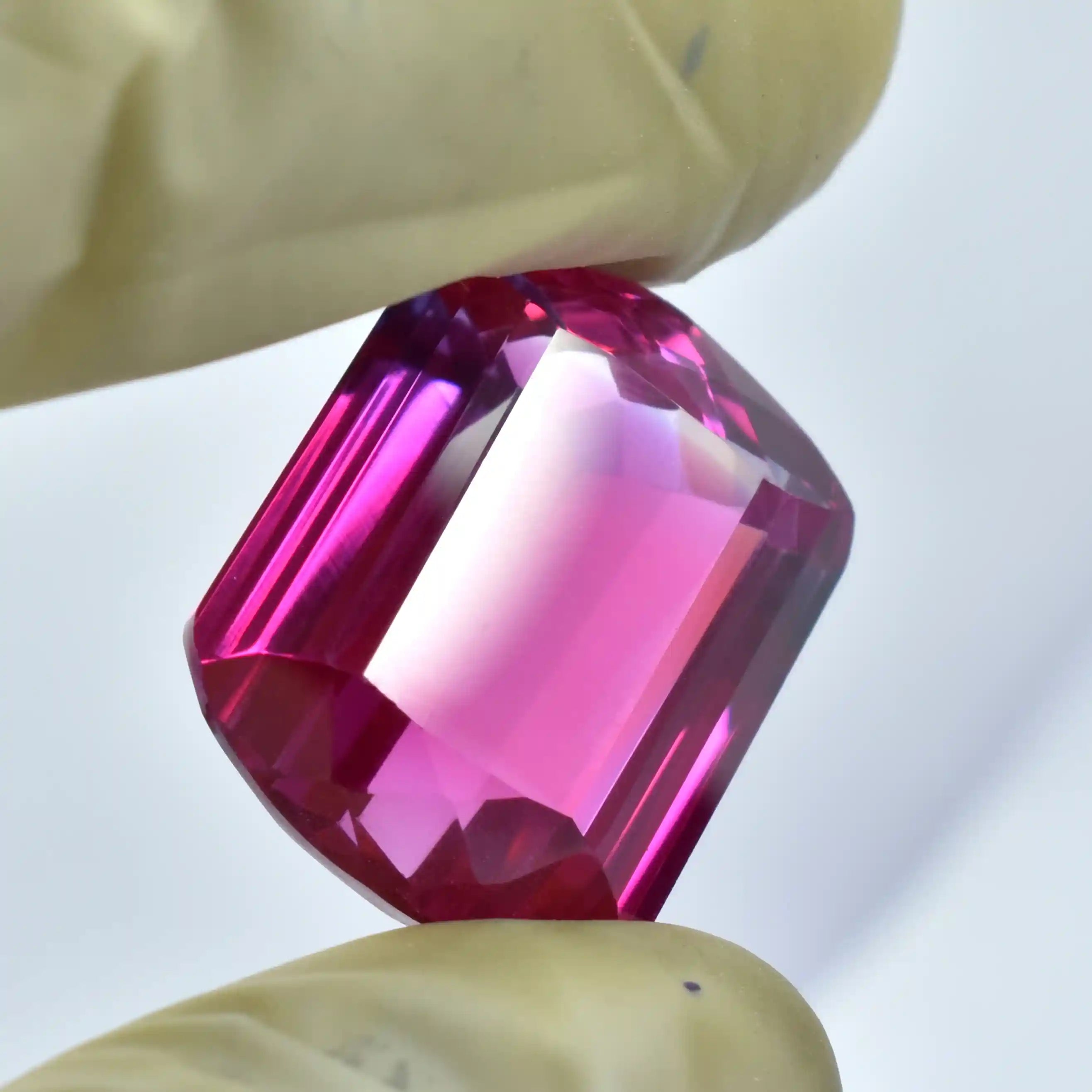Close-up of a pink gemstone held between tweezers with a blurred background