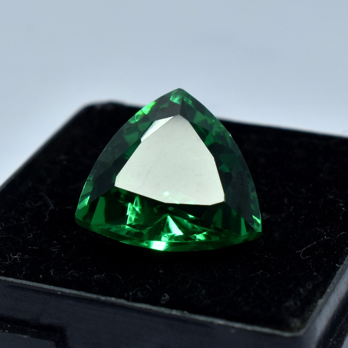 10.65 Ct Green Tsavorite Garnet displayed on a black box with white background, clarity enhanced trillion cut