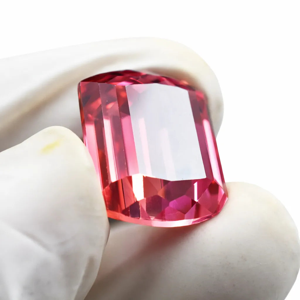 Faceted red gemstone held between white gloves on a white background