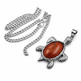 Silver turtle pendant with a red stone on a white background
