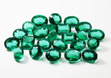 A set of lab-created green Muzo emeralds, including oval, circular, and rectangular shapes, arranged at the center in a white display, showcasing transparency and excellent cut.