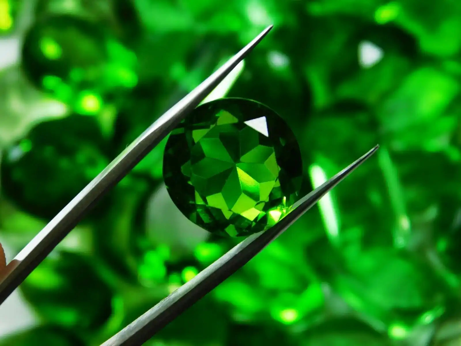 Green gemstone held by tweezers against a green background